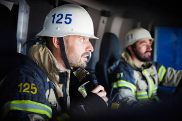 Feuerwehrmann spricht mit Mikrofon, während er mit einem Kollegen im Feuerwehrauto sitzt - MASF14164