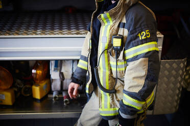 Midsection of firefighter with walkie-talkie walking at fire station - MASF14166