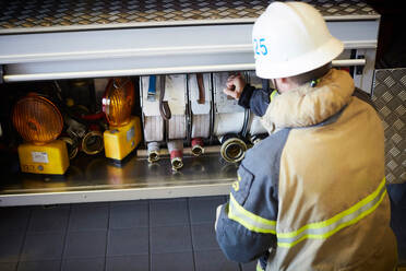 Rear view of firefighter arranging fire hose in engine at fire station - MASF14167