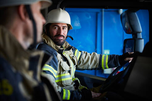 Feuerwehrmann sieht seinen Kollegen an, während er im Feuerwehrauto sitzt - MASF14168