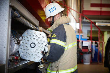 Side view of firefighter arranging fire hose in fire engine at station - MASF14169