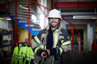 Porträt eines lächelnden Feuerwehrmanns mit Schutzanzug auf der Feuerwache - MASF14172