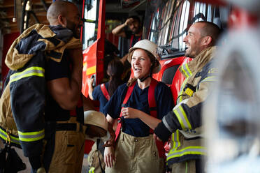 Fröhliche Feuerwehrleute unterhalten sich, während sie an einem Feuerwehrauto in der Feuerwache stehen - MASF14173