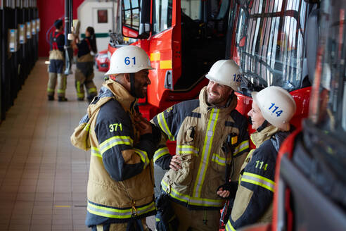 Mitarbeiter lächelnd vor einem Feuerwehrauto in der Feuerwache stehend - MASF14174