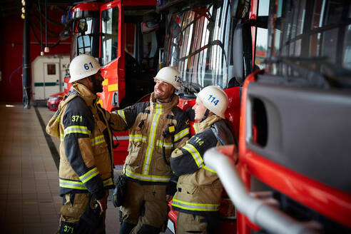 Eine Gruppe von Feuerwehrleuten unterhält sich auf der Feuerwache mit einem Löschfahrzeug - MASF14175