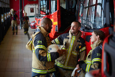 Firefighters in uniform talking while standing at fire station - MASF14176