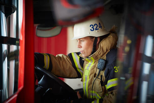 Weiblicher Feuerwehrmann mit Helm im Feuerwehrauto auf der Feuerwache sitzend - MASF14177