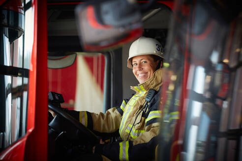 Porträt einer lächelnden Feuerwehrfrau, die in einem Feuerwehrauto auf der Feuerwache sitzt - MASF14179