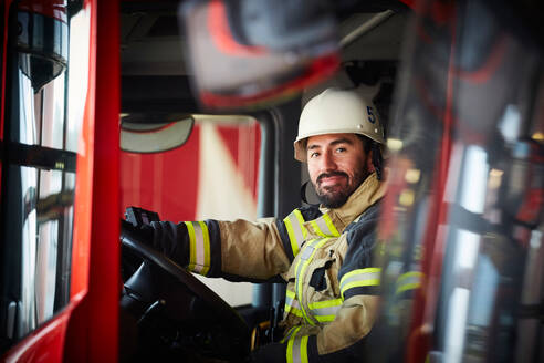 Porträt eines selbstbewussten männlichen Feuerwehrmannes, der in einem Feuerwehrauto auf der Feuerwache sitzt - MASF14181