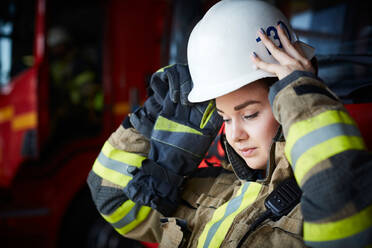 Weiblicher Feuerwehrmann mit Helm und Blick auf die Feuerwache - MASF14184
