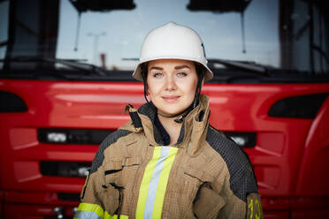 Porträt eines weiblichen Feuerwehrmanns mit Helm vor einem Löschfahrzeug auf einer Feuerwache - MASF14185