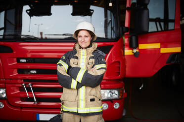 Portrait of confident female firefighter standing with arms crossed against fire engine at fire station - MASF14188