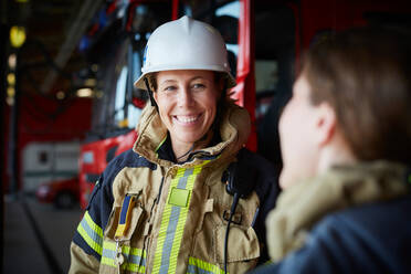 Lächelnder weiblicher Feuerwehrmann, der einen Kollegen in der Feuerwache anschaut - MASF14191