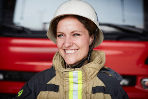 Lächelnder weiblicher Feuerwehrmann mit Helm, der in der Feuerwache wegschaut - MASF14192