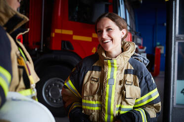 Lächelnder weiblicher Feuerwehrmann, der einen Kollegen ansieht, während er in der Feuerwache kommuniziert - MASF14193