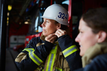 Weiblicher Feuerwehrmann trägt Helm, während er mit einem Kollegen in der Feuerwache steht - MASF14194
