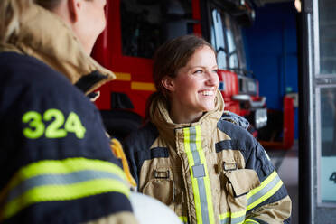 Smiling female firefighter standing with coworker in fire station - MASF14195