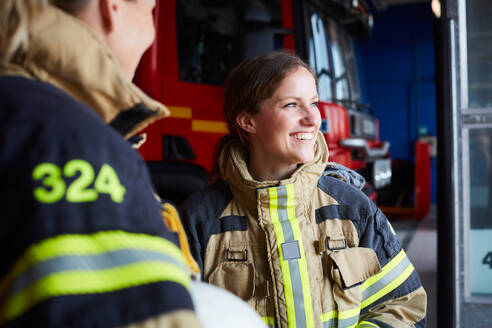 Lächelnder weiblicher Feuerwehrmann, der mit einem Kollegen in einer Feuerwache steht - MASF14195