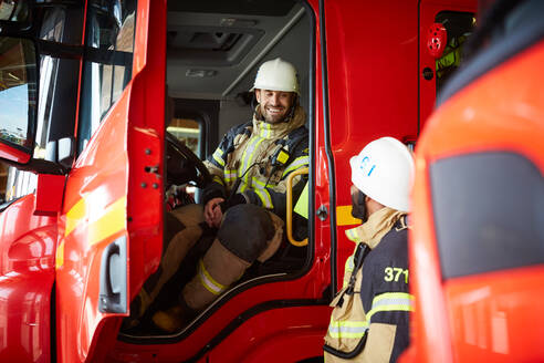 Feuerwehrmann im Gespräch mit einem Kollegen, während er im Feuerwehrauto auf der Feuerwache sitzt - MASF14197