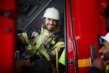 Lächelnder Feuerwehrmann, der im Feuerwehrauto sitzt und sich mit einem Kollegen unterhält - MASF14198