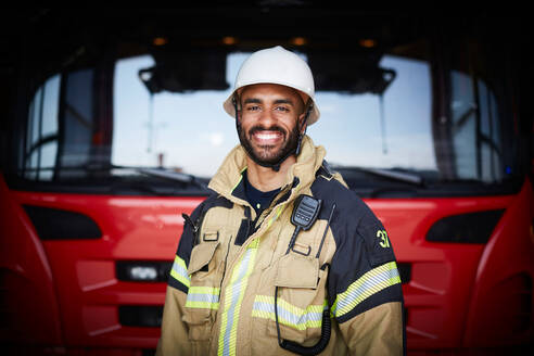 Porträt eines lächelnden Feuerwehrmanns vor einem Feuerwehrauto auf der Feuerwache - MASF14202