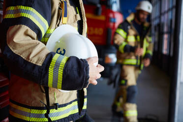 Midsection of female firefighter with protective helmet standing at fire station - MASF14206