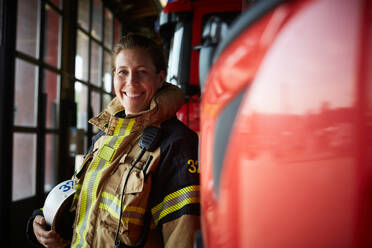 Porträt einer lächelnden Feuerwehrfrau neben einem Löschfahrzeug auf der Feuerwache - MASF14208