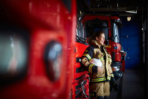 Lächelnder weiblicher Feuerwehrmann neben einem Löschfahrzeug auf der Feuerwache - MASF14212