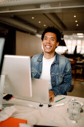 Smiling young male employee using laptop while looking away at desk in office - MASF14242
