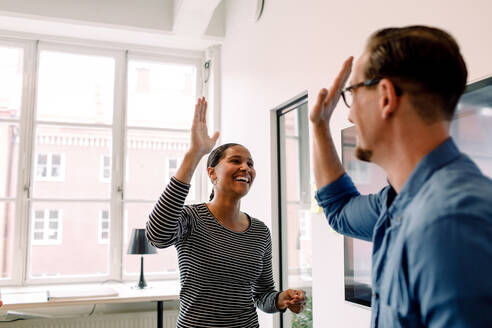 Happy businesswoman giving high-five to male colleague in office - MASF14254