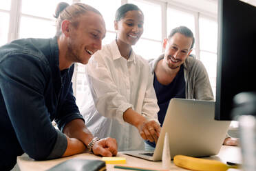 Lächelnde Mitarbeiter, die beim Diskutieren im Büro auf den Laptop schauen - MASF14274