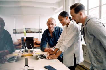 Businesswoman using laptop while discussing with male coworkers at desk in office - MASF14277