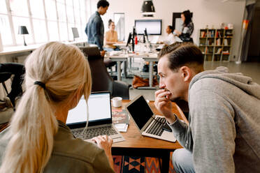 Male and female professionals working over laptop while sitting at office desk - MASF14291