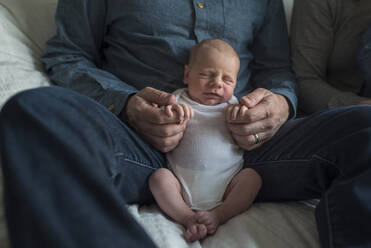 Mittelteil eines Vaters, der mit einem neugeborenen Jungen auf dem Sofa sitzt - CAVF68382