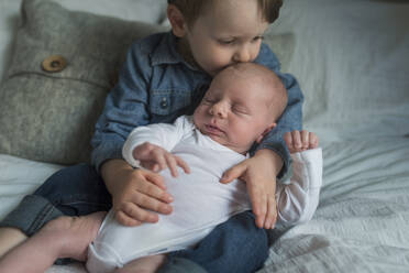 Boy kissing newborn brother on bed at home - CAVF68386