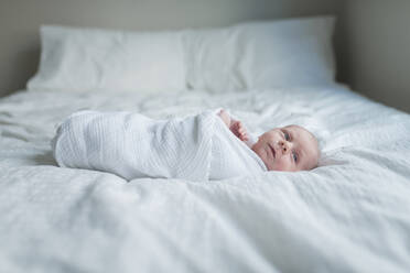 Side view of newborn baby boy looking away while lying in bed at home - CAVF68390