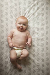 Overhead portrait of baby boy lying on bed at home - CAVF68409