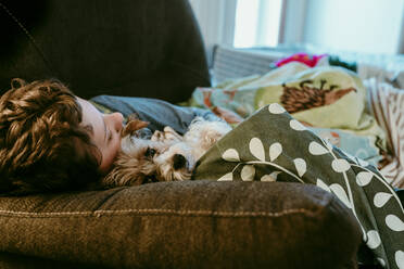 Boy and dog sleeping on sofa at home - CAVF68413