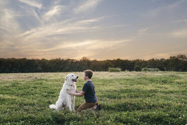 Junge mit Hund auf grasbewachsenem Feld gegen bewölkten Himmel bei Sonnenuntergang - CAVF68445