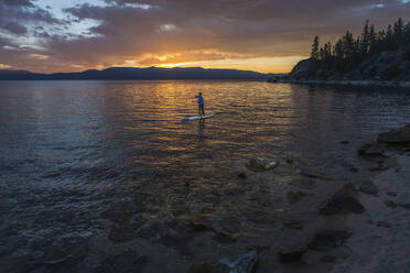 Mann paddelt bei Sonnenuntergang auf einem See - CAVF68469