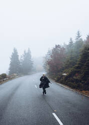 Rear view of woman running on road against sky during foggy weather - CAVF68477