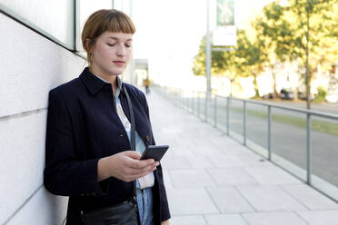 Portrait of strawberry blonde young woman looking at cell phone - FLLF00336