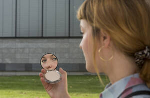 Junge Frau mit Nasenpiercing betrachtet den Schönheitsspiegel in ihrer Hand - FLLF00341