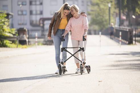 Granddaughter assisting her grandmother walking with wheeled walker - UUF19503