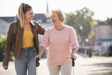 Granddaughter assisting her grandmother walking with wheeled walker - UUF19505