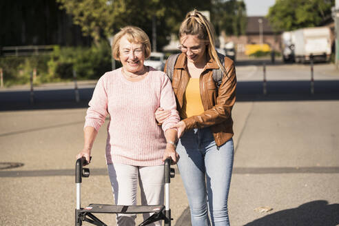 Granddaughter assisting her grandmother walking with wheeled walker - UUF19506