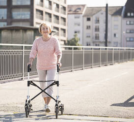 Senior woman with wheeled walker on footbridge - UUF19520