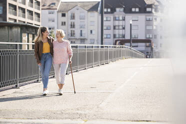 Granddaughter and her grandmother walking on footbridge - UUF19527