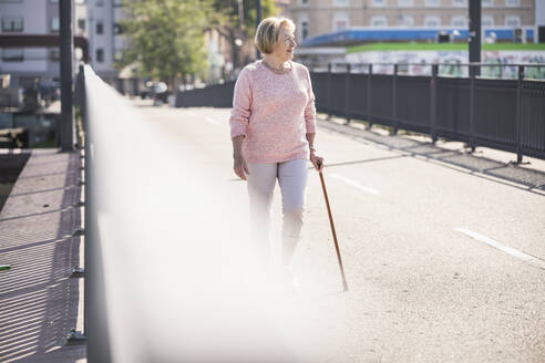 Ältere Frau, die auf einer Fußgängerbrücke geht und einen Gehstock benutzt - UUF19534