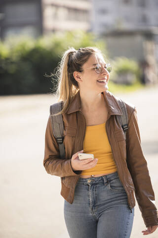 Young woman holding smartphone and looking sideways stock photo